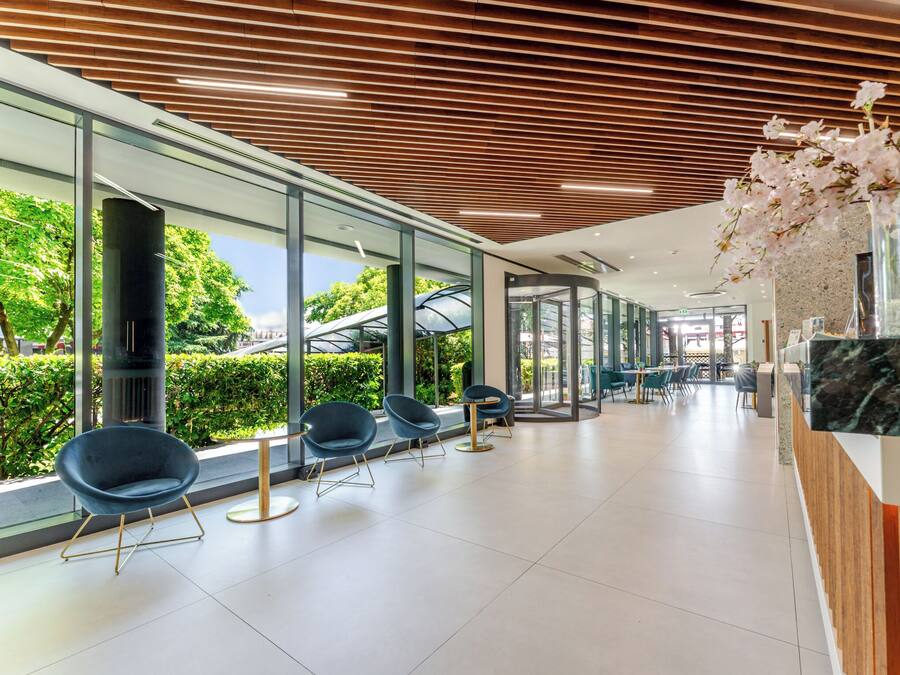 A modern interior with glass walls, wooden ceiling slats, and seating areas.