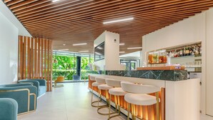 Zona de bar moderna con techo de madera, taburetes y un área de estar con sillas azules.