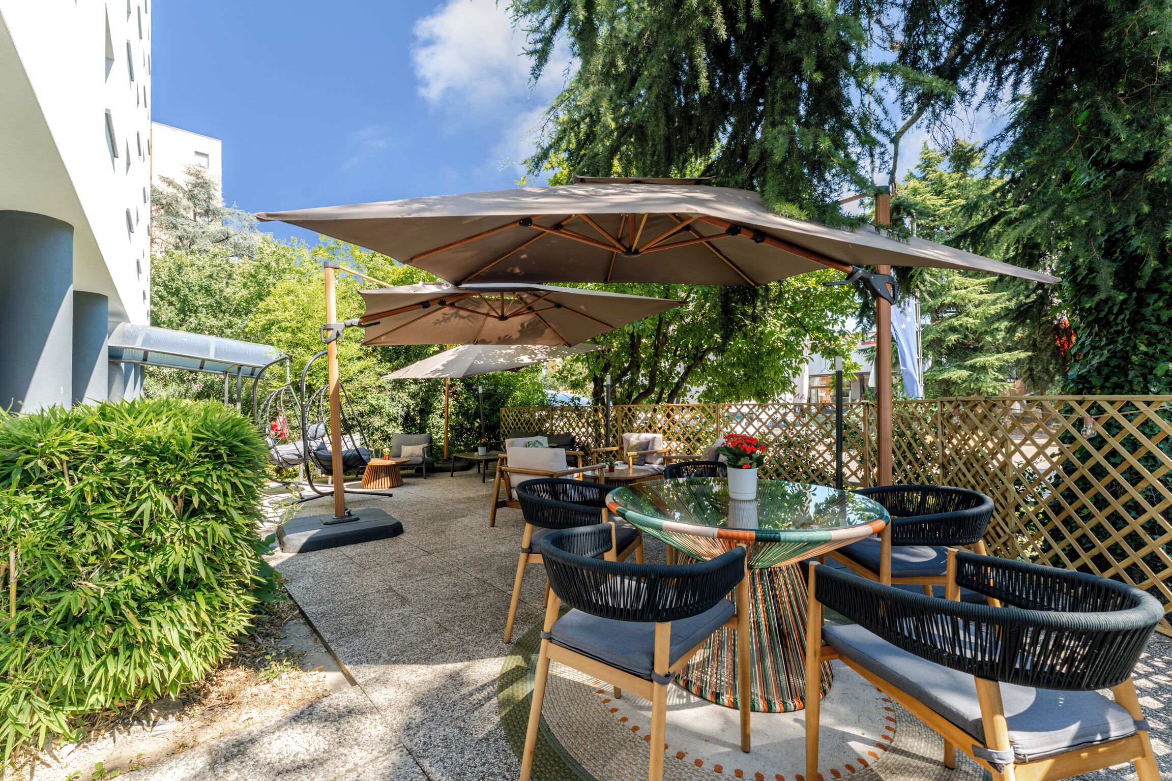 Un patio al aire libre con mesa de vidrio, sillas de mimbre y grandes sombrillas.