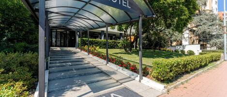 Entrada de un hotel con un vestíbulo cubierto, escalones que conducen a la entrada y un letrero que dice 'AOCa HOTEL'.