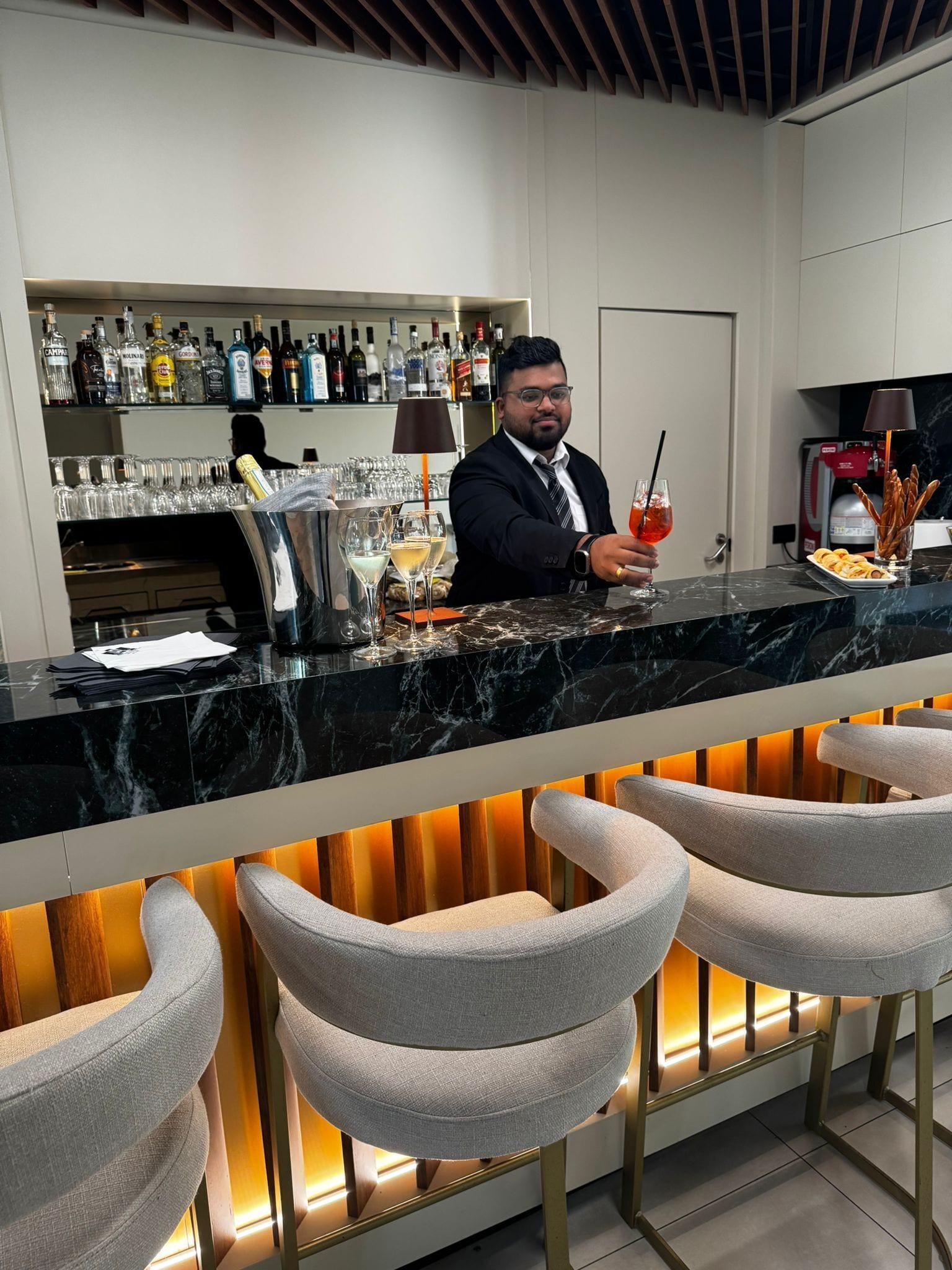 Un espace bar doté d’un comptoir en marbre, de tabourets de bar et d’une variété de bouteilles d’alcool.