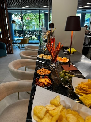 Una mesa de buffet con diversas opciones de bocadillos y bebidas, rodeada de sillas modernas y vista a zonas verdes al exterior.