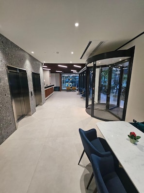 Un moderno vestíbulo de hotel con un mostrador de recepción, zona de estar y puertas de vidrio que dan a un espacio exterior.
