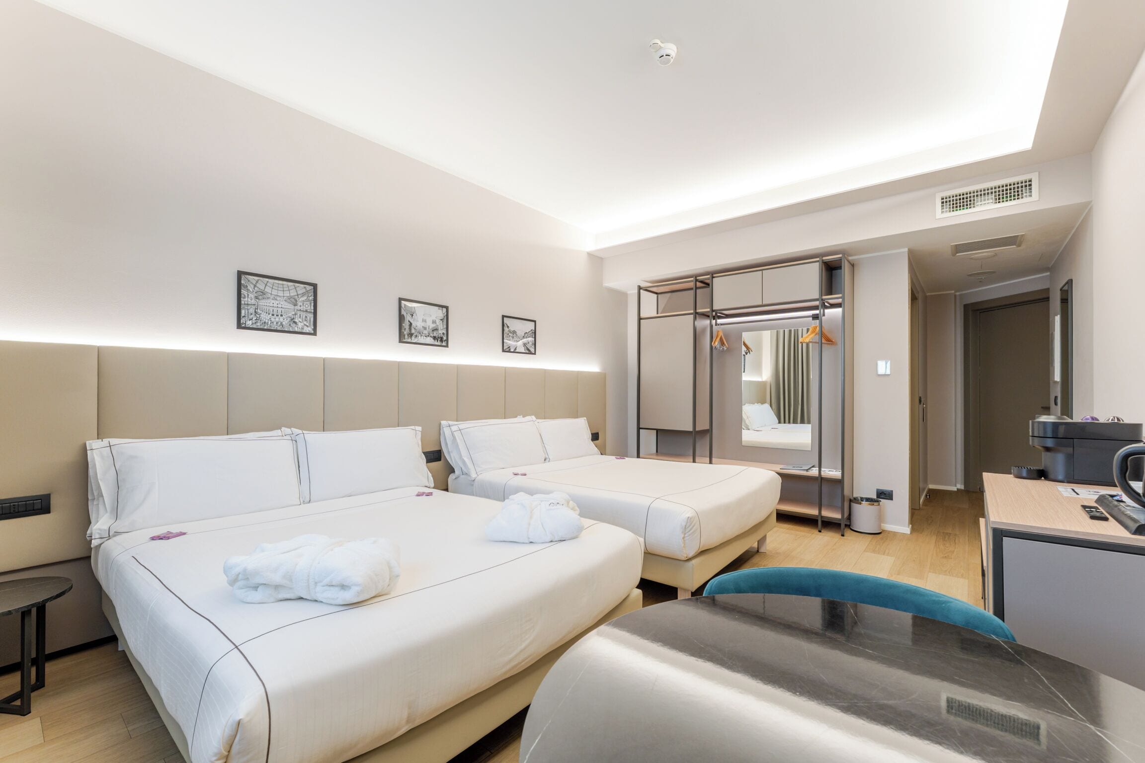 A hotel room with two beds, a desk, a chair, a wardrobe, and a mirror.