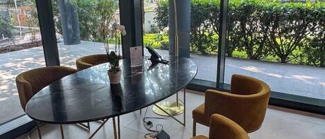 Une salle de conférence moderne, dotée d’une table ronde et de quatre chaises, de grandes fenêtres offrant une vue sur la verdure et les bâtiments, ainsi que d’un luminaire suspendu.