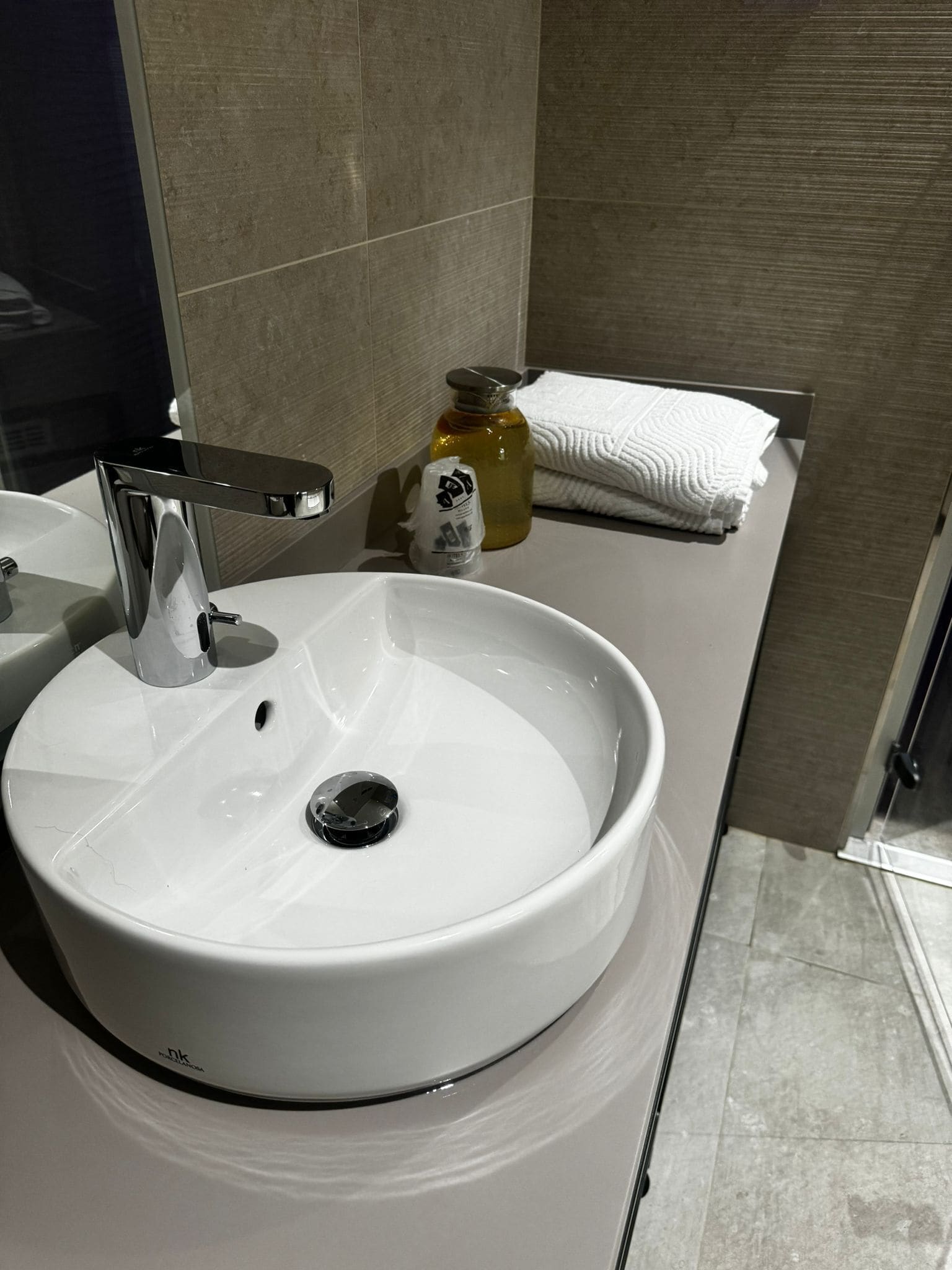 A white bathroom sink with a chrome faucet, a soap dispenser, and a bottle of liquid soap on the countertop.