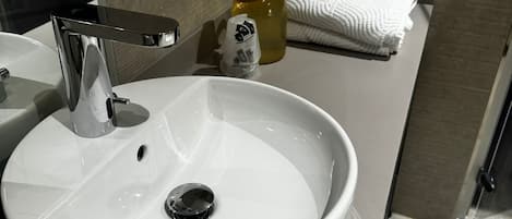 A white bathroom sink with a chrome faucet, a soap dispenser, and a bottle of liquid soap on the countertop.