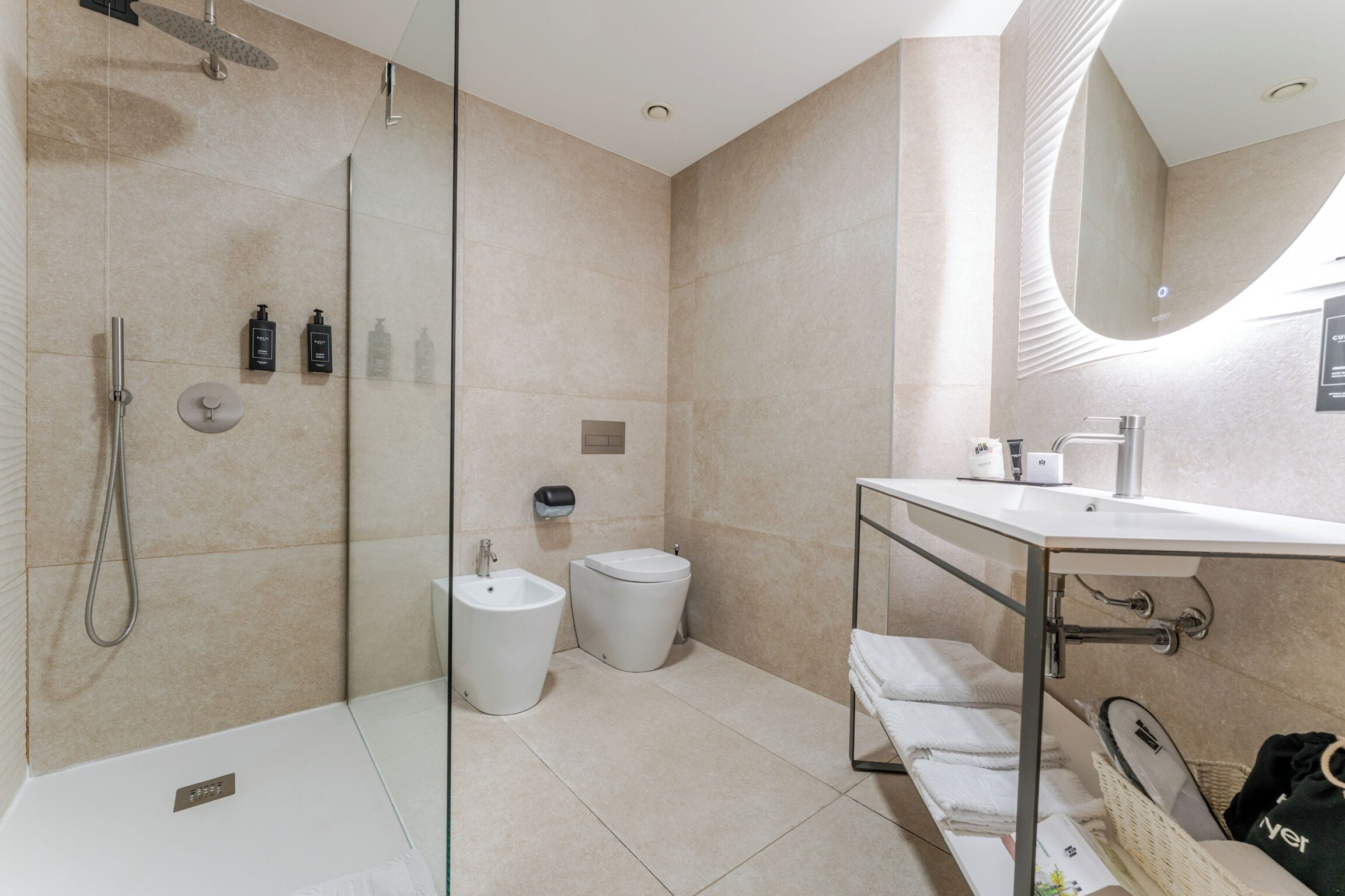 Et moderne badeværelse med en glas brusekabine, et bidet, et toilet, en vask med spejl og en bøjle til håndklæder.