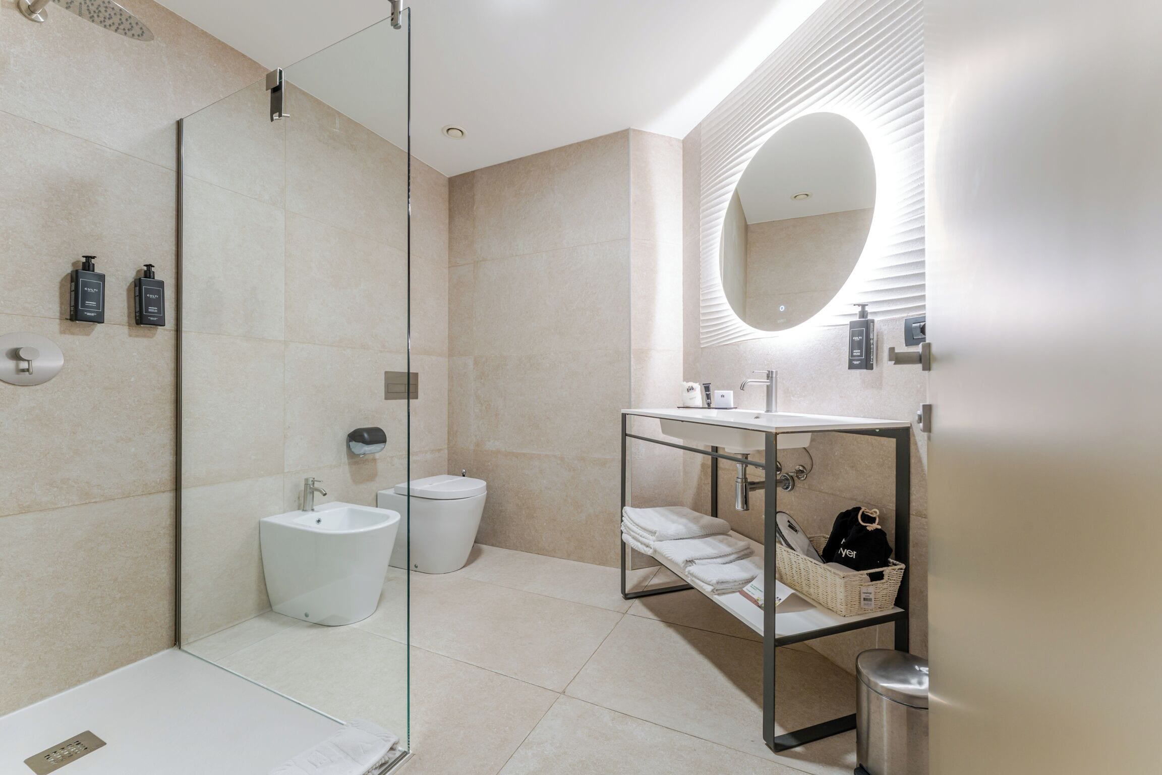 A modern bathroom with a glass shower enclosure, a bidet, a sink with a mirror, and a towel rack.