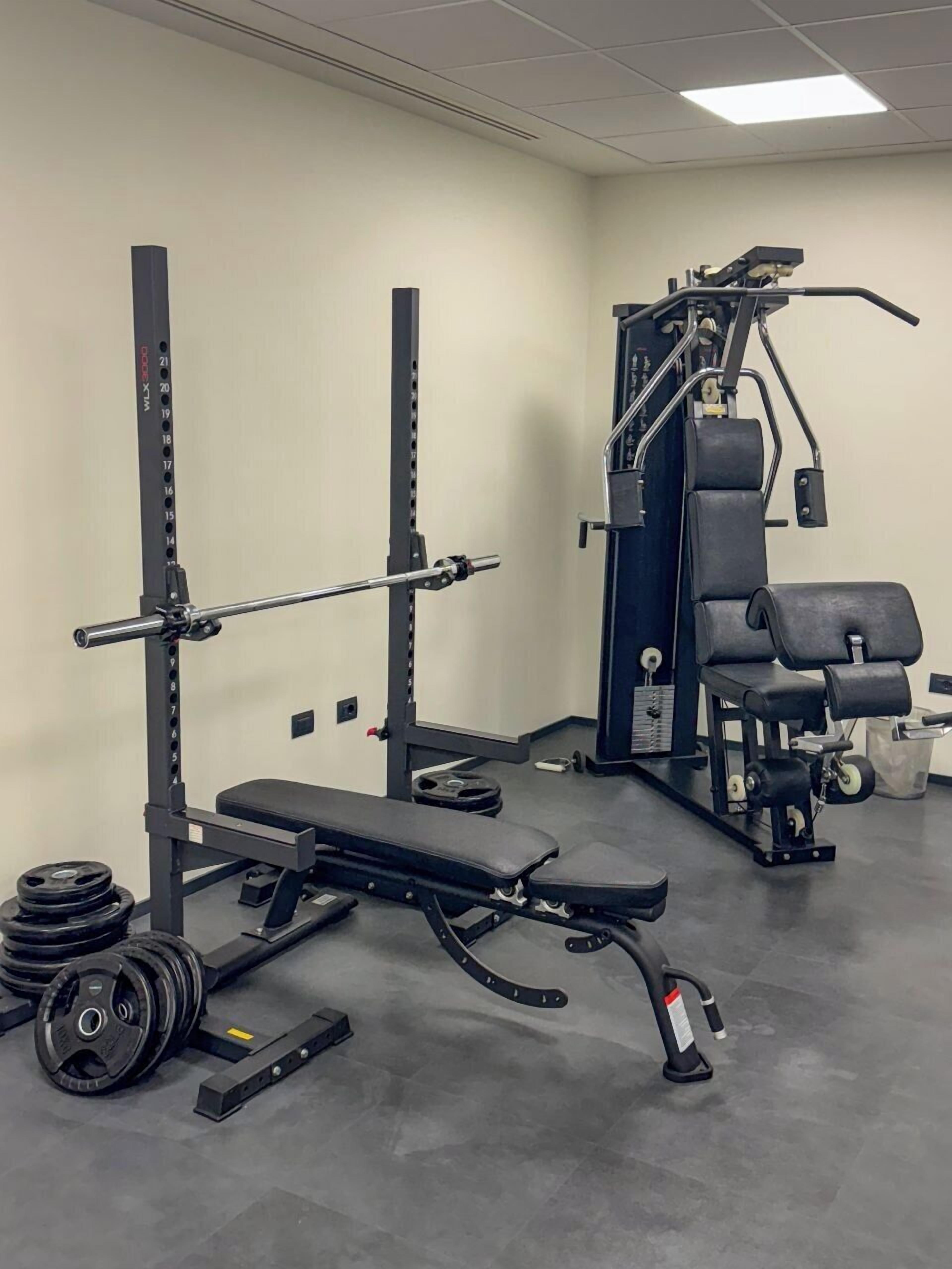 Une salle de sport équipée de matériel de musculation, notamment un banc de développé couché, un support à squats et divers poids.