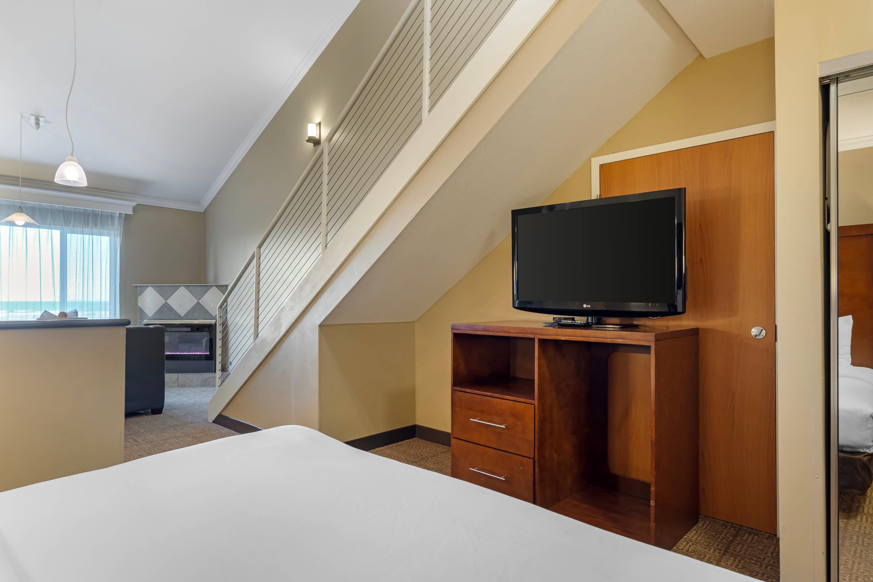 A hotel room with a bed, a TV on a wooden stand, a desk, and a staircase.