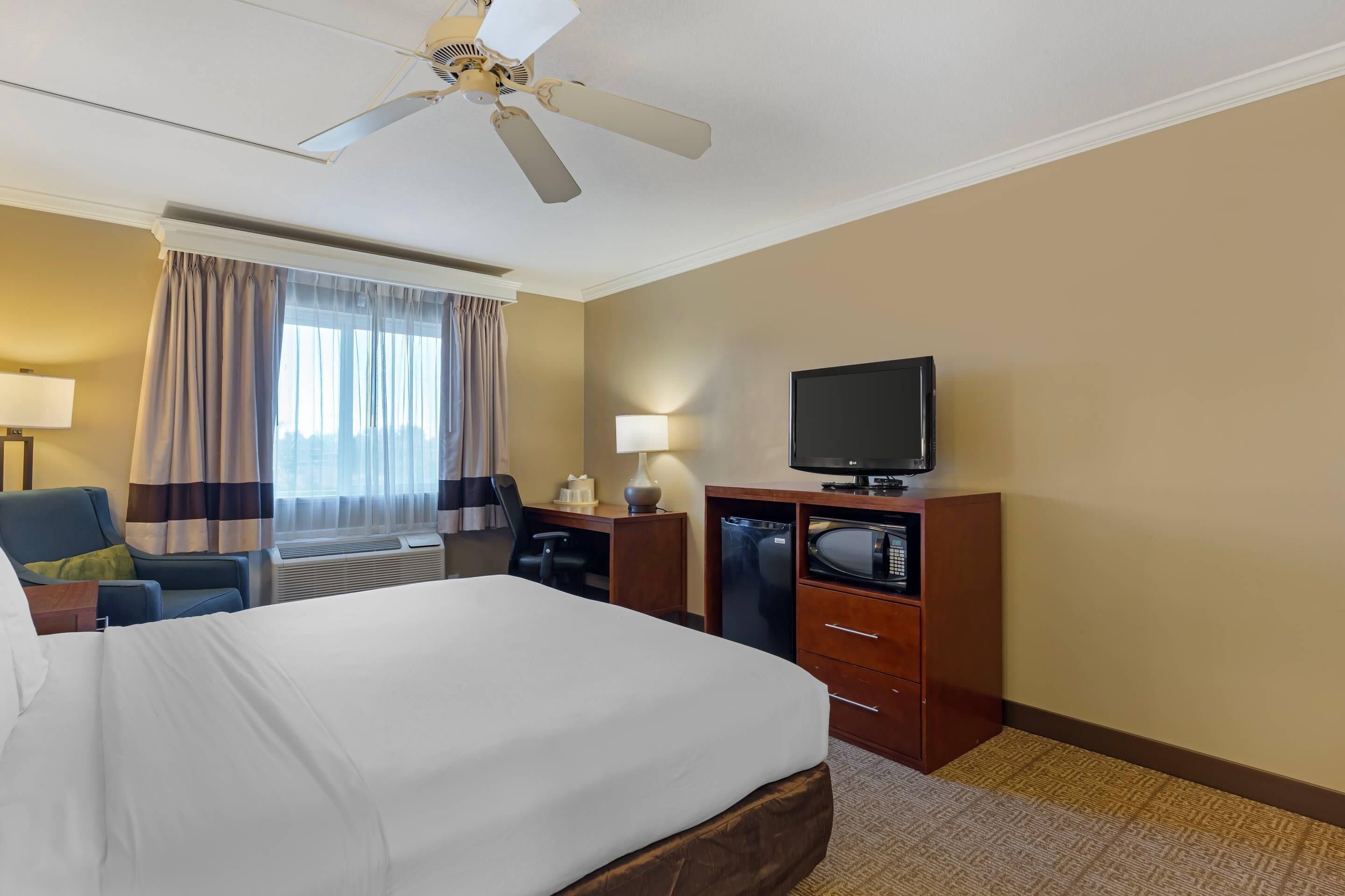 Ein Hotelzimmer mit einem großen Bett, einem Schreibtisch mit Stuhl, einem Fernseher, einer Mikrowelle und einem Deckenventilator.