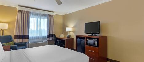 Ein Hotelzimmer mit einem großen Bett, einem Schreibtisch mit Stuhl, einem Fernseher, einer Mikrowelle und einem Deckenventilator.