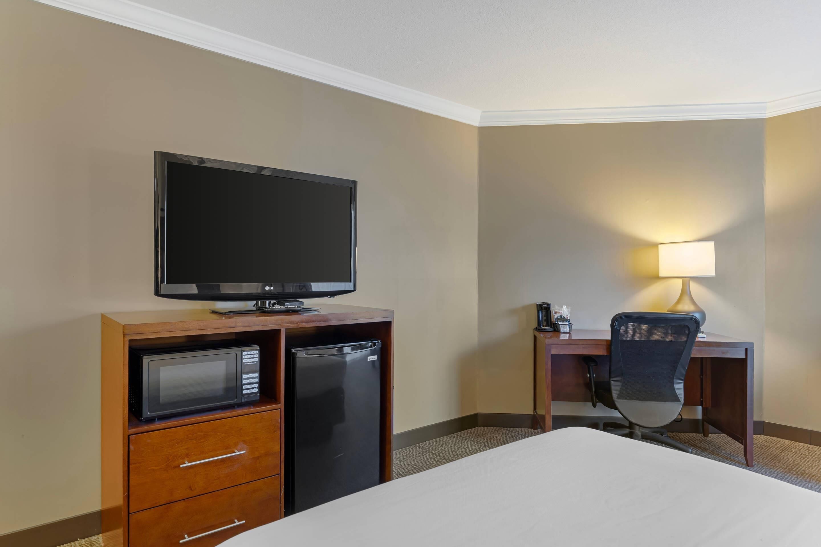 Una habitación de hotel con una cama, un escritorio con silla, televisor, microondas y refrigerador.