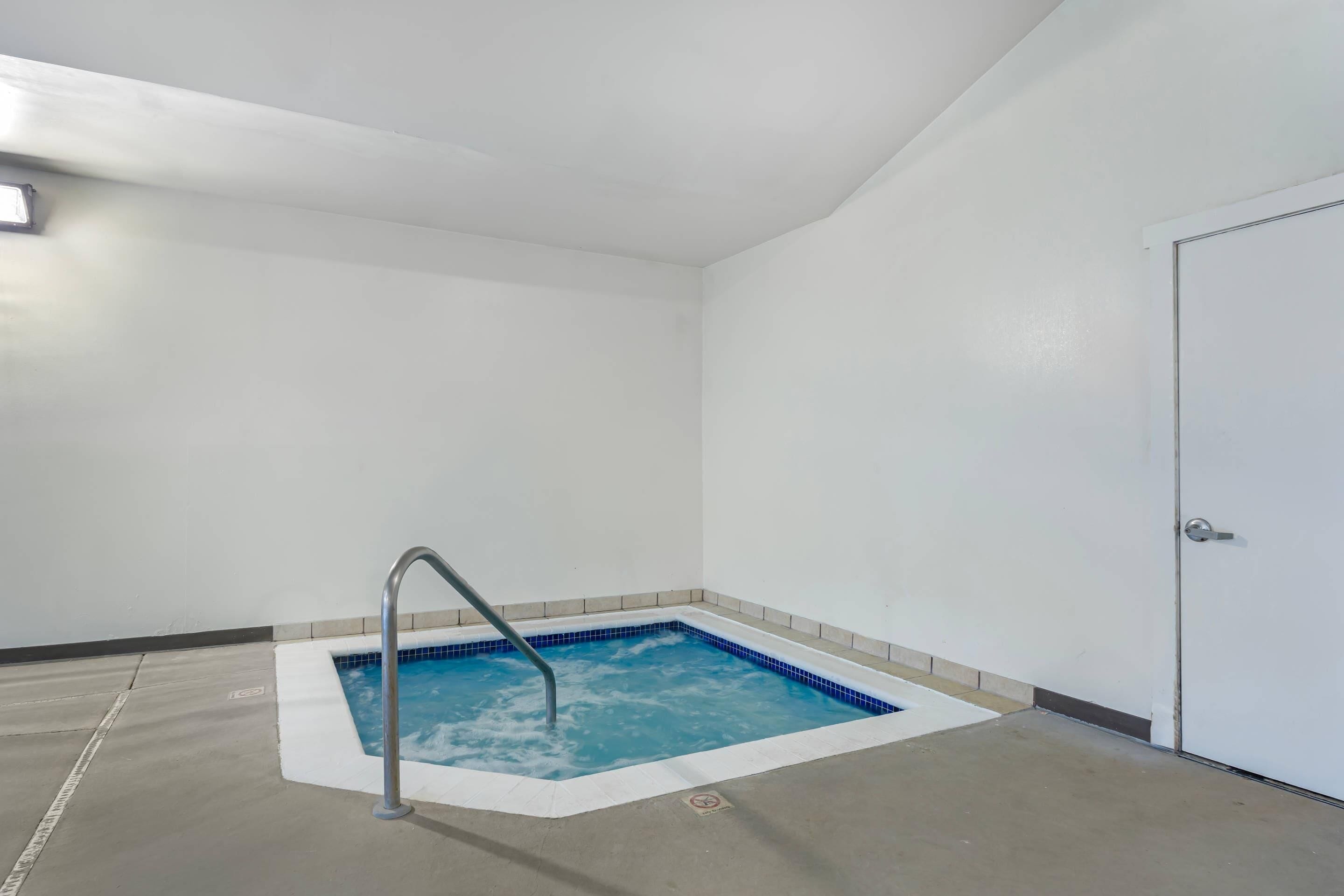 Un petit bain à remous carré, doté d’une échelle en métal, entouré de murs blancs et posé sur un sol carrelé.
