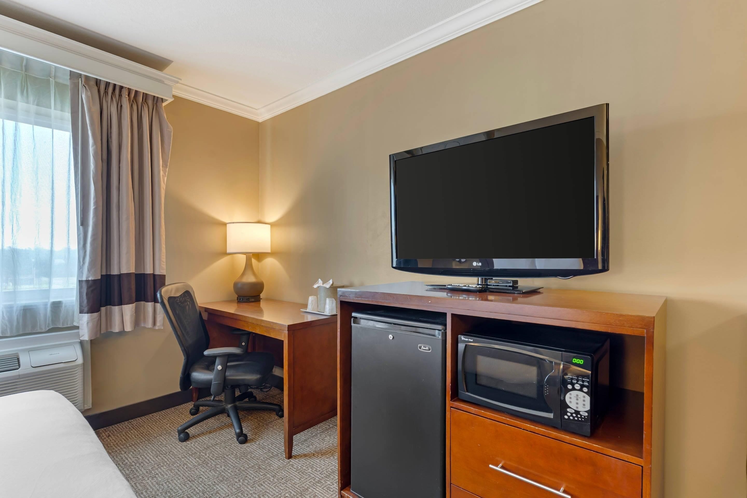 Habitación de hotel con cama, escritorio, silla, televisor, refrigerador y microondas.