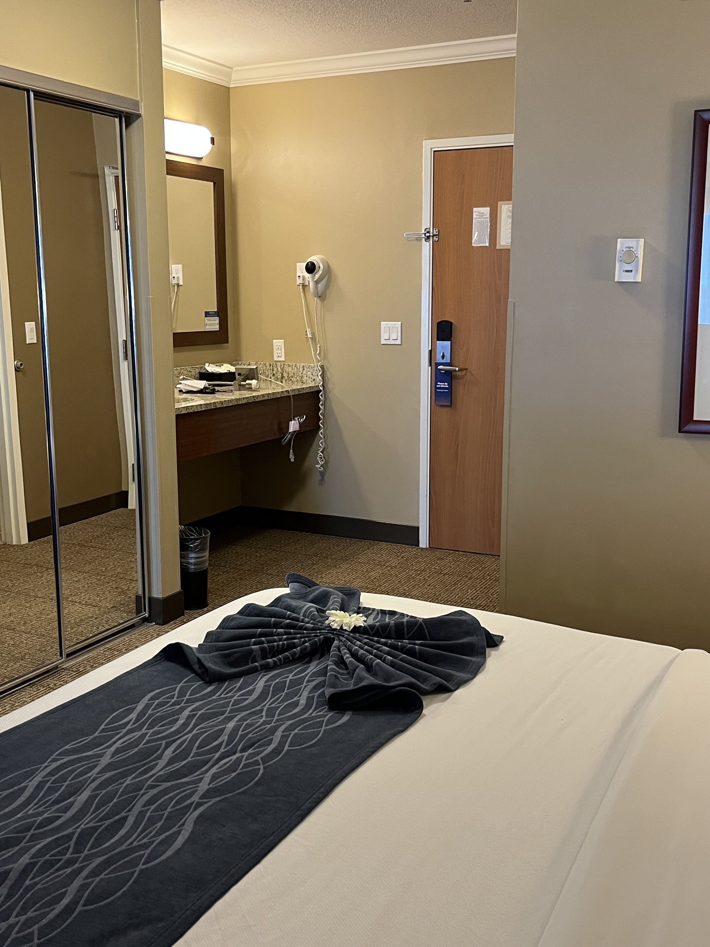 Quarto de hotel com uma cama, banheiro com espelho, secador de cabelo e porta.