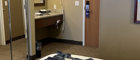 A hotel room with a bed, a bathroom with a mirror, a hairdryer, and a door.