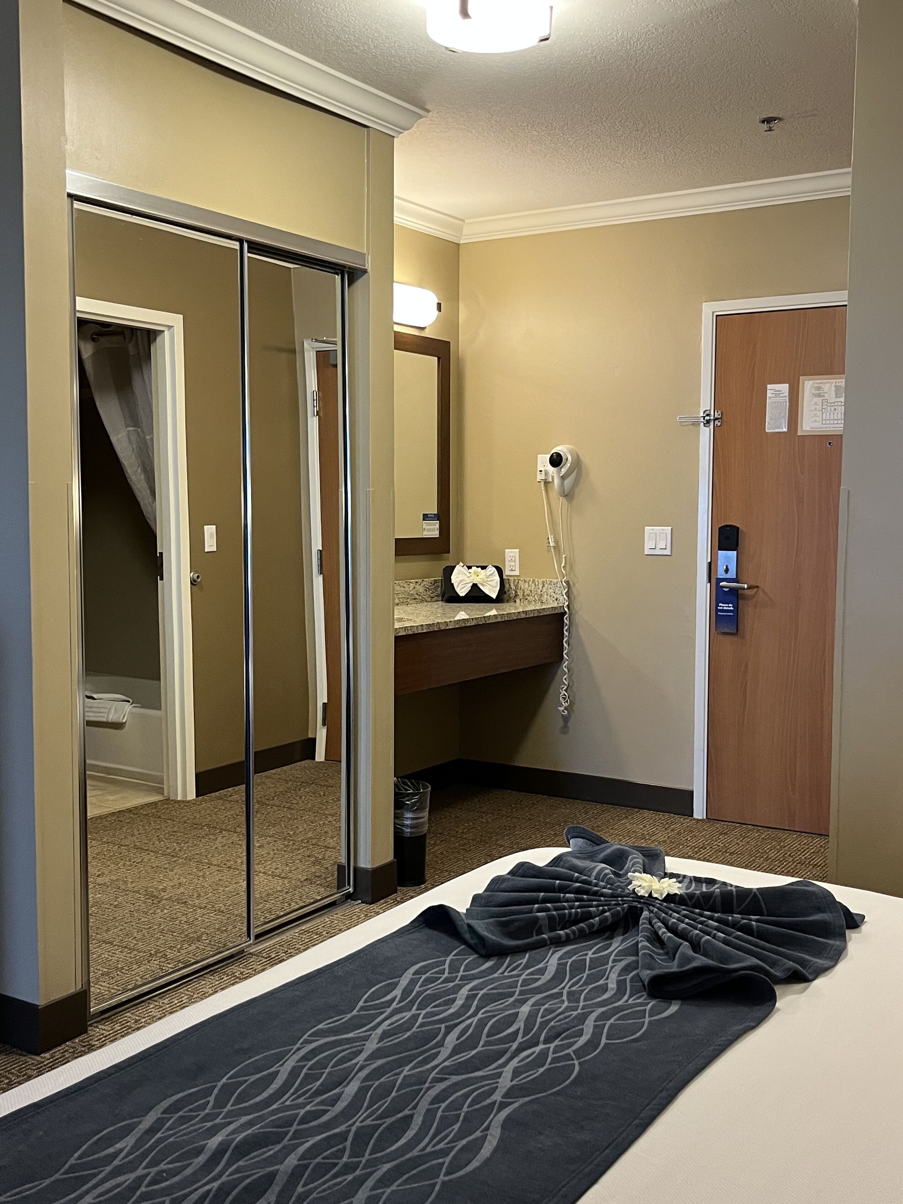 A hotel room with a bed, a bathroom, a mirror, and a hairdryer.