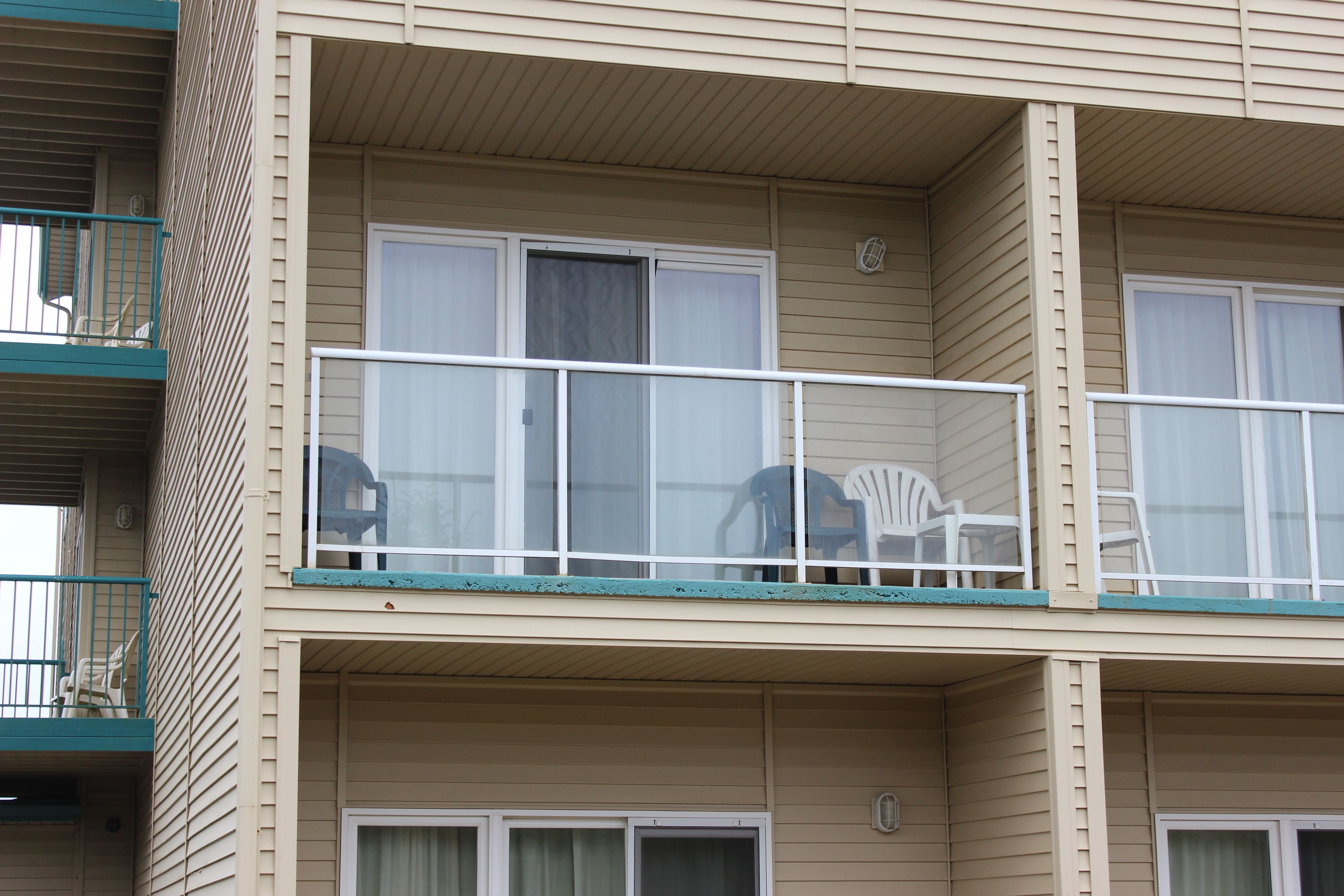 A multi-story building with balconies, each with a railing and a chair.