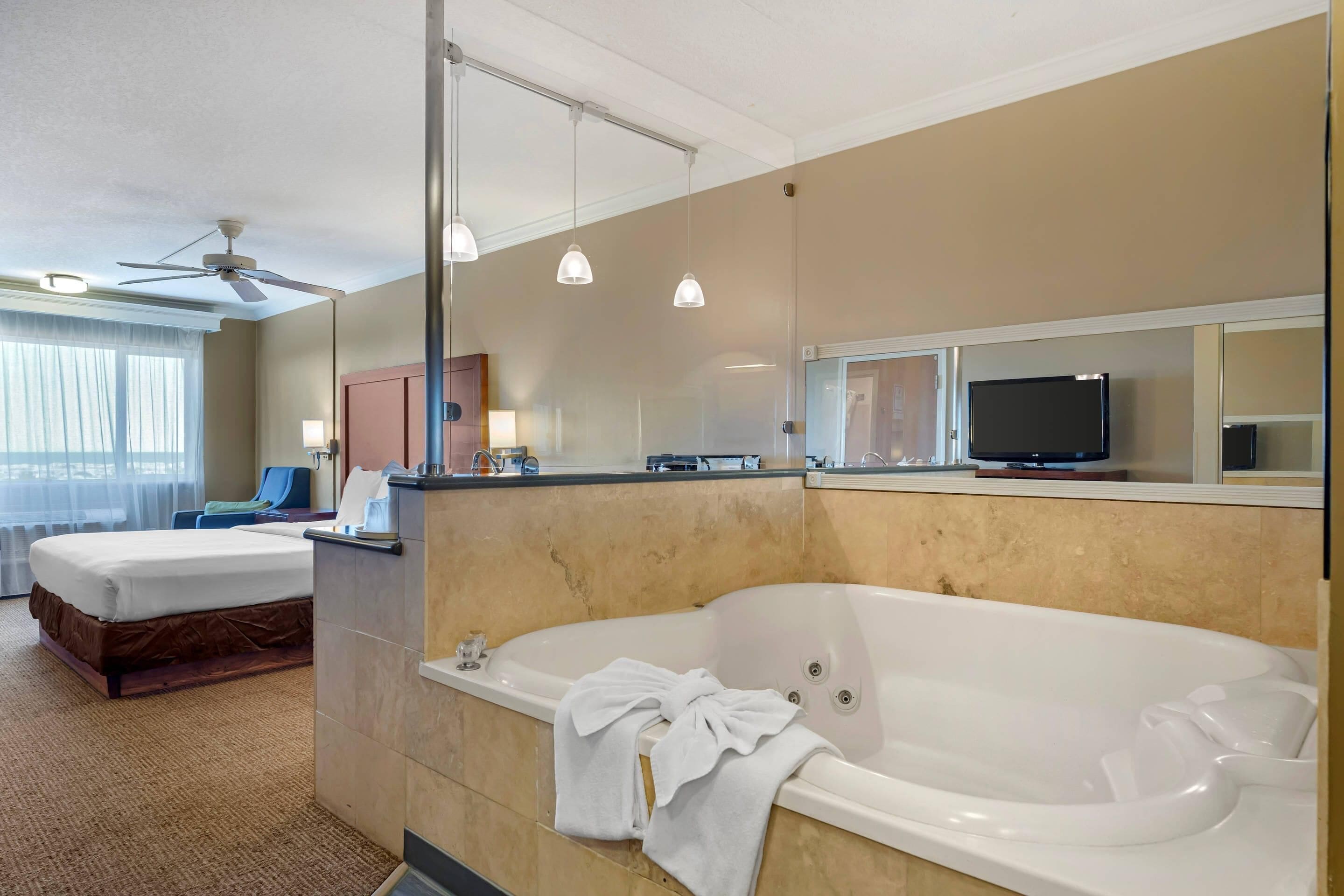 A hotel room with a large bathtub, a bed, a desk with a mirror, and a television.