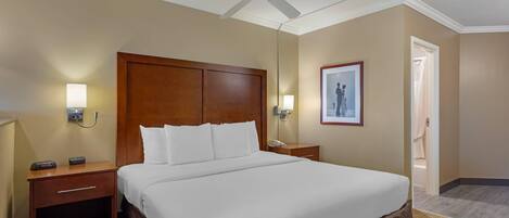 Habitación de hotel con una cama grande, cabecera de madera, mesitas de noche con lámparas, ventilador de techo y un cuadro en la pared.