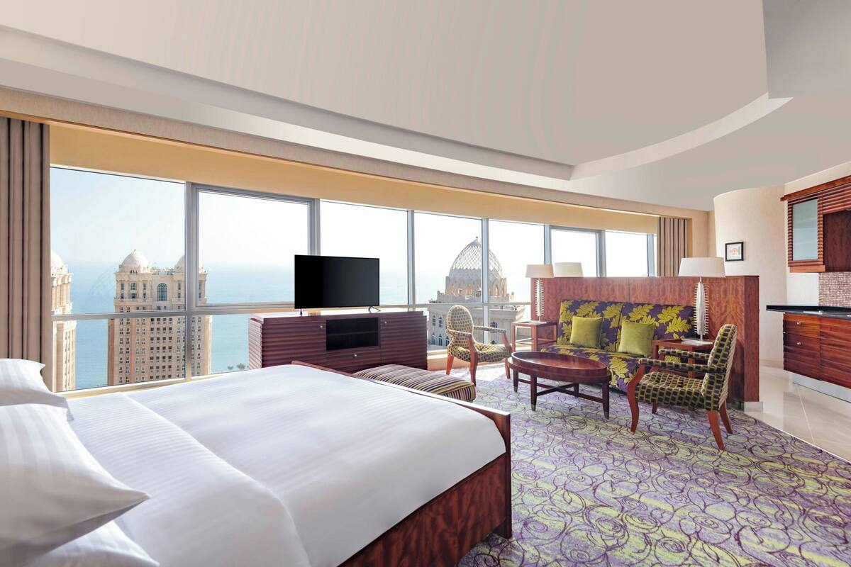 Una habitación de hotel con una cama grande, televisión, sofá y vista a un paisaje urbano.