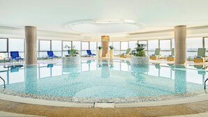 An indoor swimming pool with clear water, surrounded by lounge chairs and potted plants. - Qabila Westbay Hotel by Marriott (Doha)