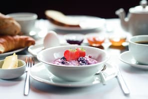 A breakfast setting with a bowl of oatmeal topped with strawberries and blueberries, accompanied by croissants and a teapot. - Qabila Westbay Hotel by Marriott (Doha)