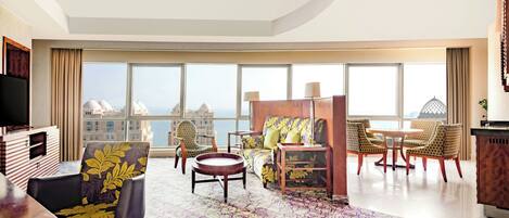 A modern hotel room with a large window offering a city view, a cozy seating area with a sofa and chairs, a flat-screen TV, and a wooden side table.