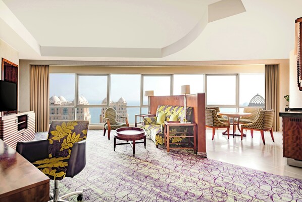 A modern hotel room with a large window offering a city view, a cozy seating area with a sofa and chairs, a flat-screen TV, and a wooden side table. - Qabila Westbay Hotel by Marriott (Doha)