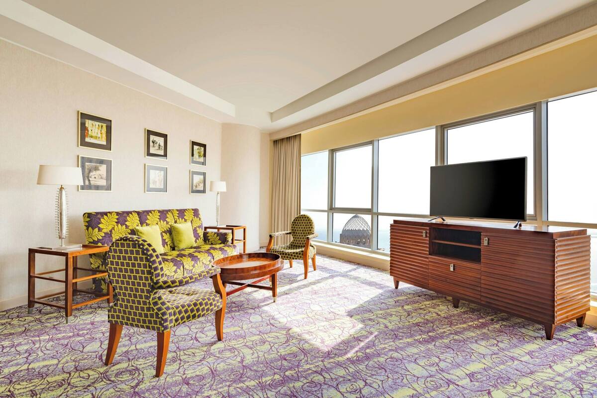 Una habitación de hotel con sofá, sillón y un mueble de madera con televisor.