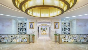 A modern hotel lobby with a central chandelier, marble walls, and a display of framed photographs. - Qabila Westbay Hotel by Marriott (Doha)