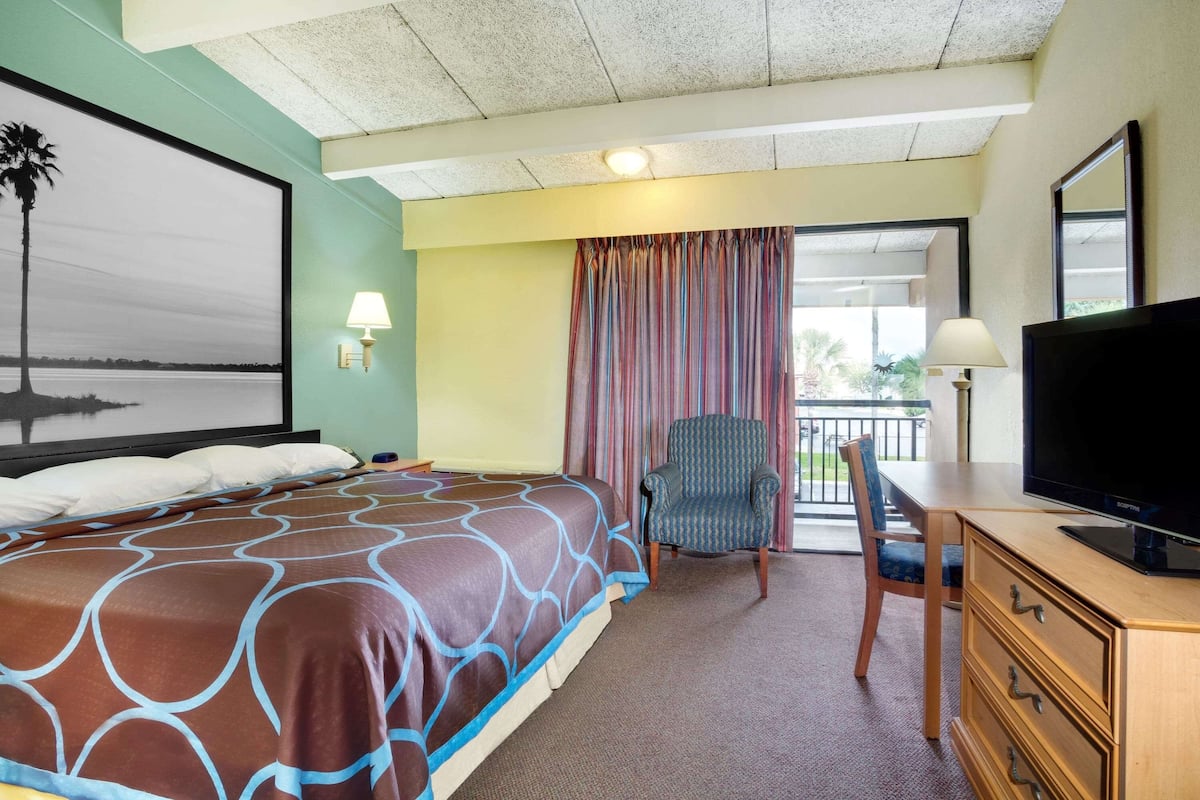 A hotel room with a bed, a desk with a television, a chair, and a balcony with curtains.