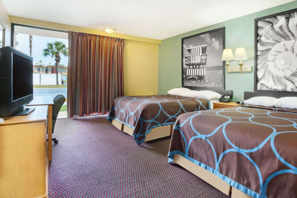 A hotel room with two beds, a television, a desk, and a window with curtains.