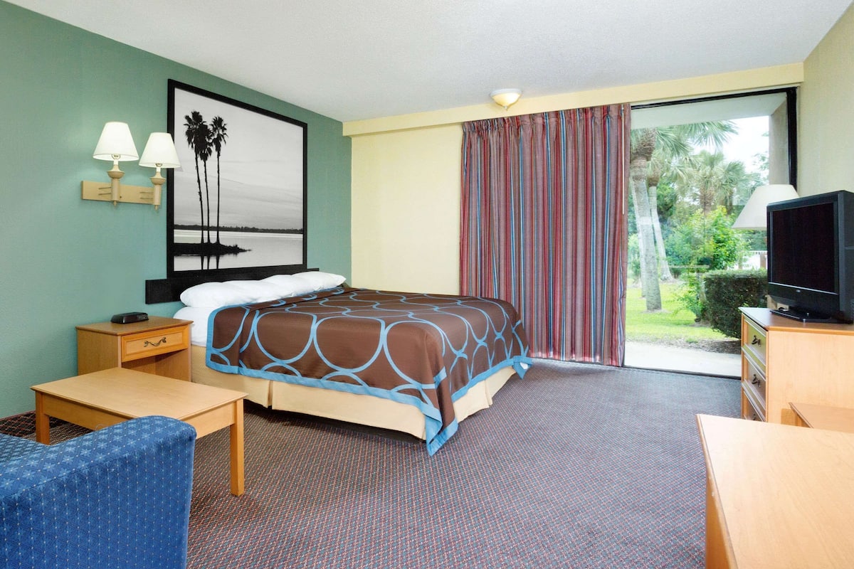 A hotel room with a bed, a desk, a chair, a television, and a window with curtains.