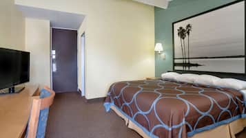 Habitación de hotel con cama, televisor sobre una mesa de madera, una puerta y un muro con un cuadro de palmeras.