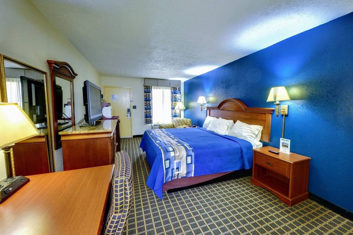 A hotel room with a bed, a desk, a chair, a mirror, and a lamp.