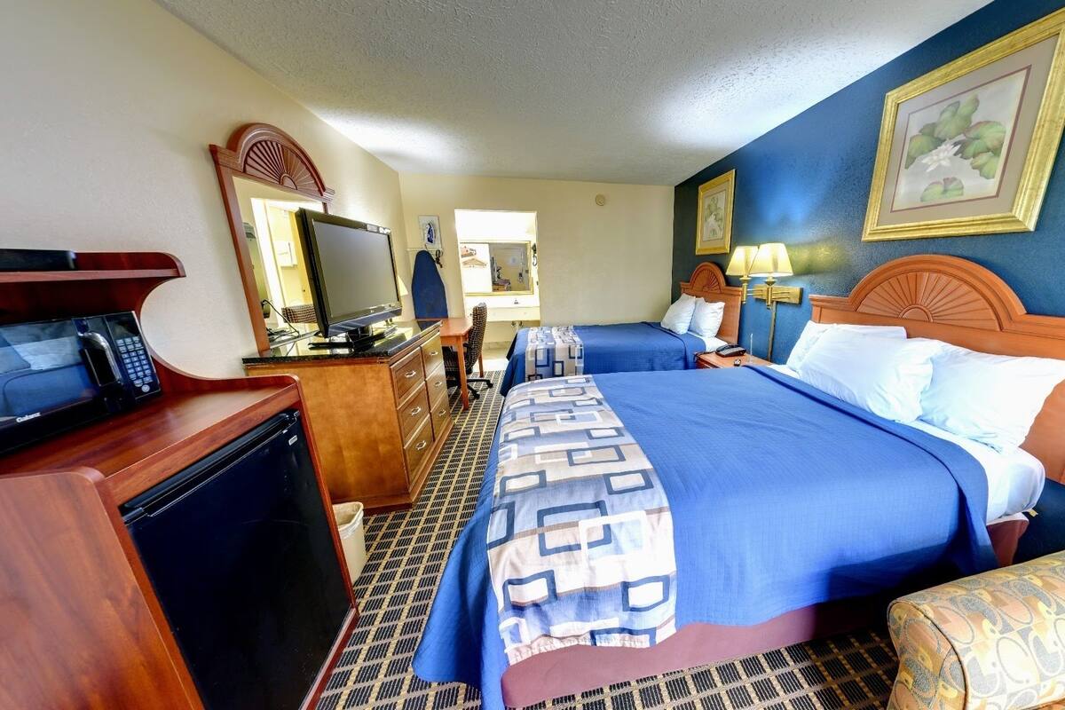 A hotel room with a large bed, a desk with a computer, a television, and a bathroom visible in the background.