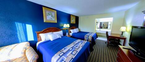 A hotel room with two beds, a desk with a computer, a TV, and a window with a view of the room.