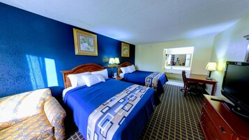 Habitación de hotel con dos camas, un escritorio con una computadora, un televisor y una ventana con vista al resto de la habitación.