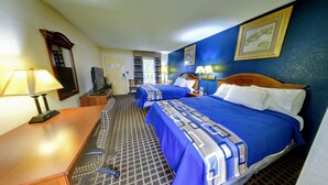 A hotel room with two beds, a desk with a lamp, a chair, a television, and a bookshelf. - Dahlonega Mountain Inn (Dahlonega)