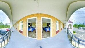 A motel with a central corridor leading to individual rooms, each with a bed and a window. There is a parking lot with several cars visible. - Dahlonega Mountain Inn (Dahlonega)