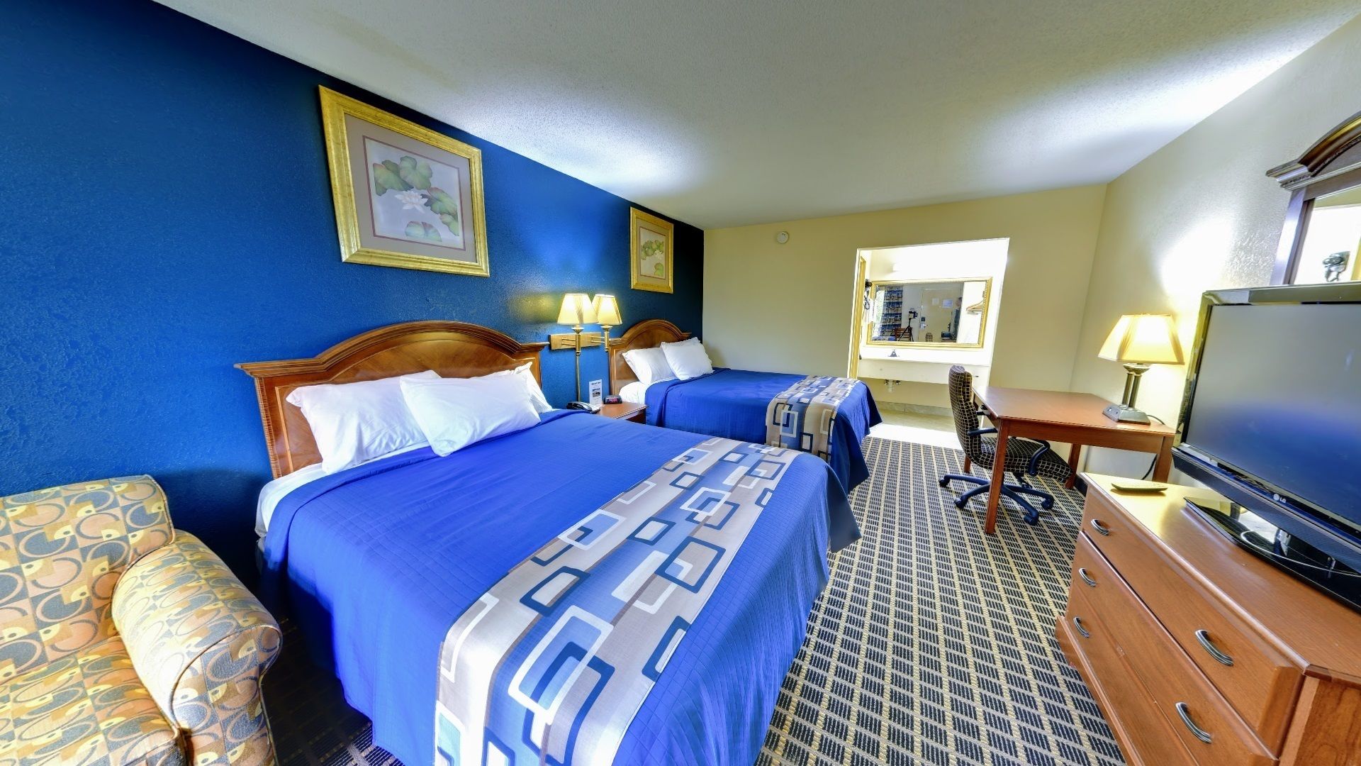 A hotel room with two beds, a desk, a television, and a bathroom visible through an open door.