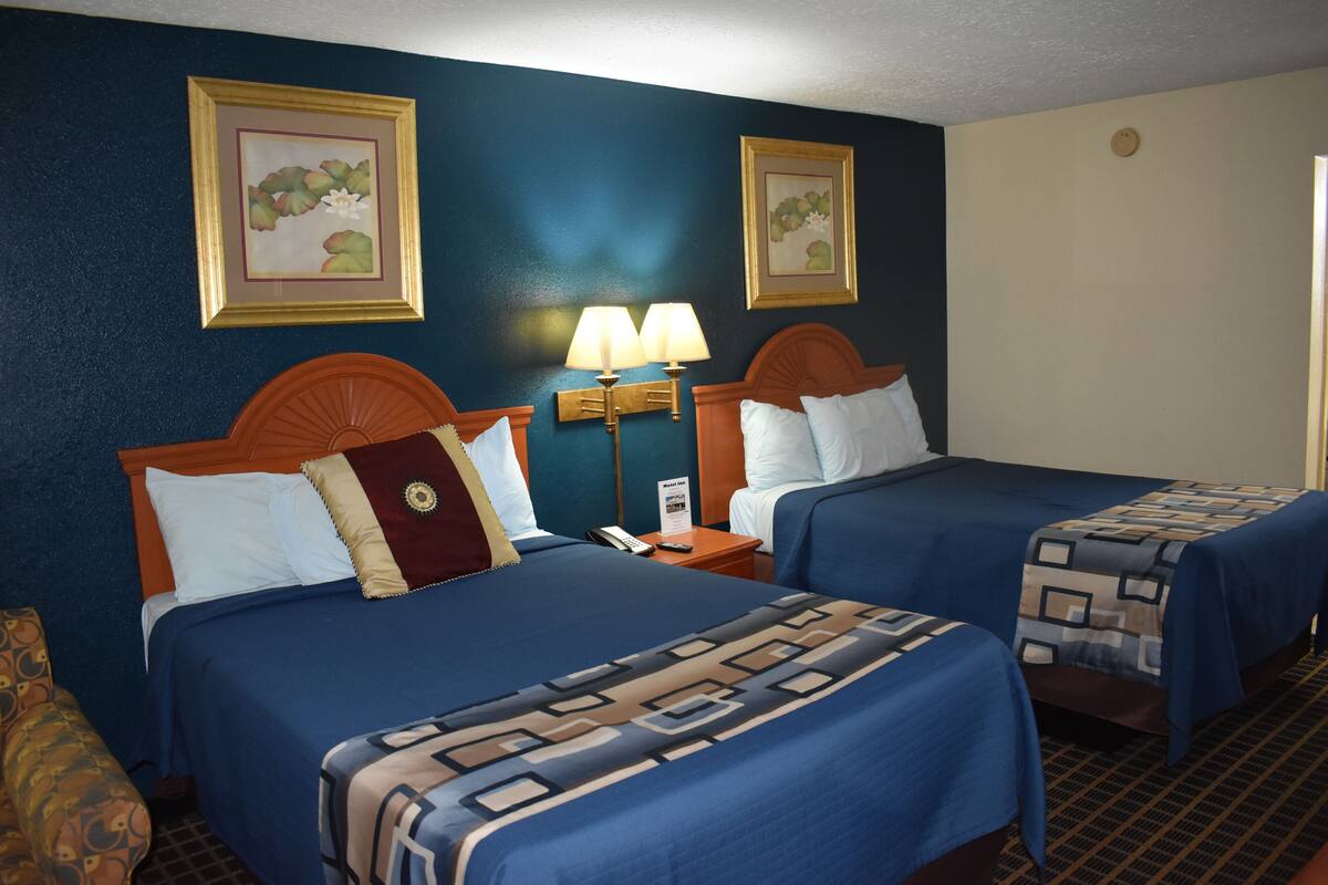 A hotel room with two beds, a nightstand with a lamp, and two framed pictures on the wall.