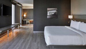 Une chambre d’hôtel moderne, dotée d’un grand lit, d’un bureau, d’une chaise, d’un téléviseur à écran plat et d’un tableau au mur.