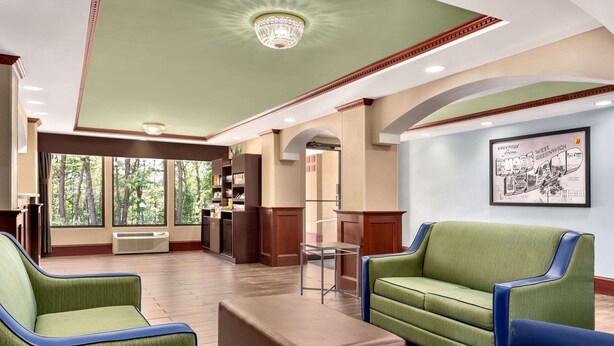 A spacious lobby with a green and blue sofa set, a wooden coffee table, and a large window offering a view of trees.