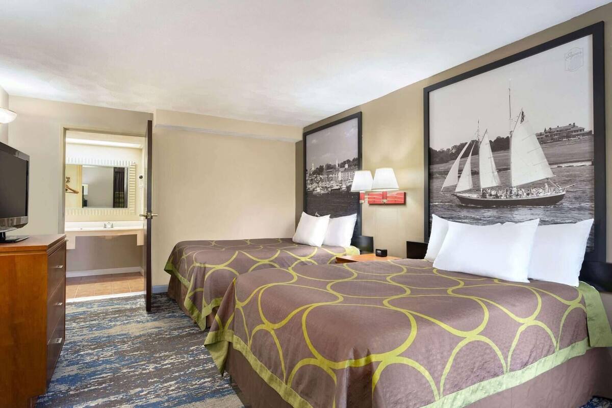 A hotel room with two beds, a television, a bathroom, and a large sailboat painting on the wall.
