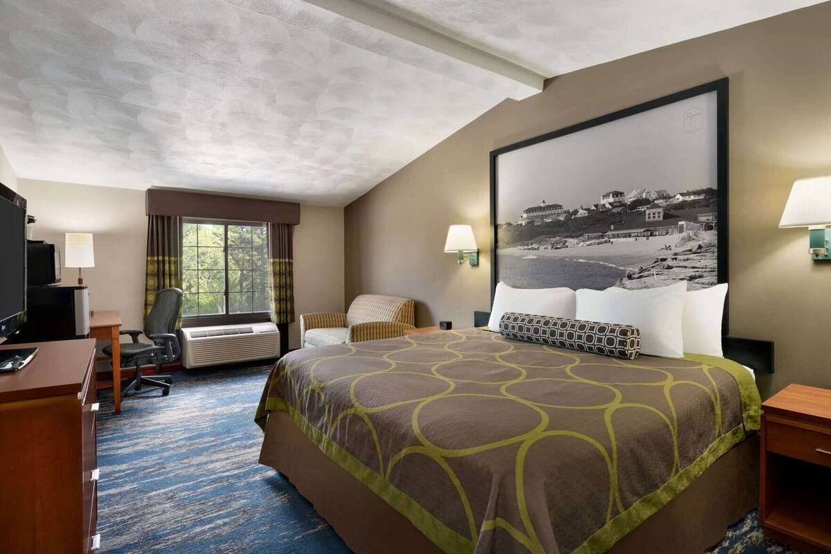 A hotel room with a large bed, a desk with a computer, a chair, a TV, and a window with curtains.