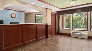 A reception area with a wooden reception desk, a clock, and a large window with a view of trees.